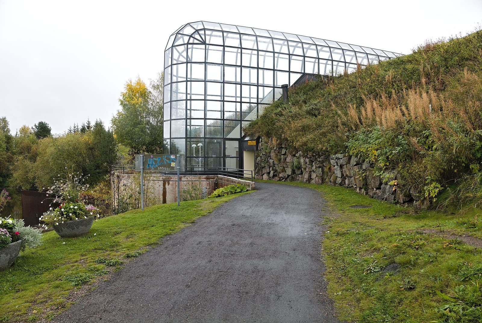 The long glass-vaulted corridor of Arktikum rising from a grassy bank beside a footpath