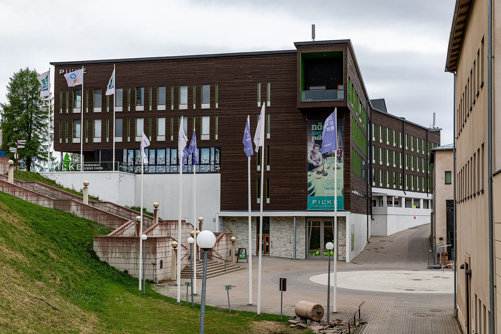 The dark timber-clad Pilke building with flags on its forecourt in Rovaniemi