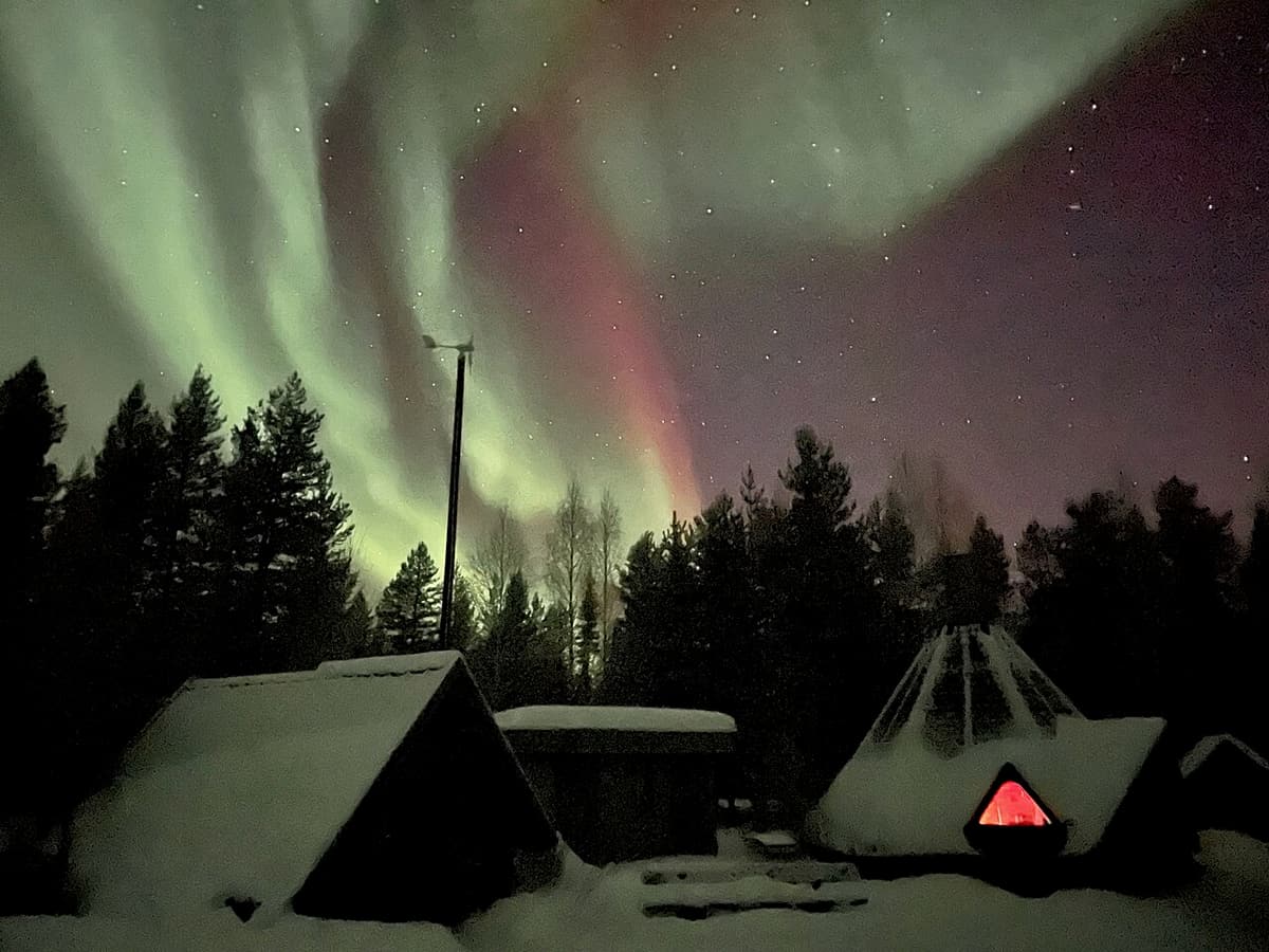 Green and red aurora above snow-covered huts in western Lapland