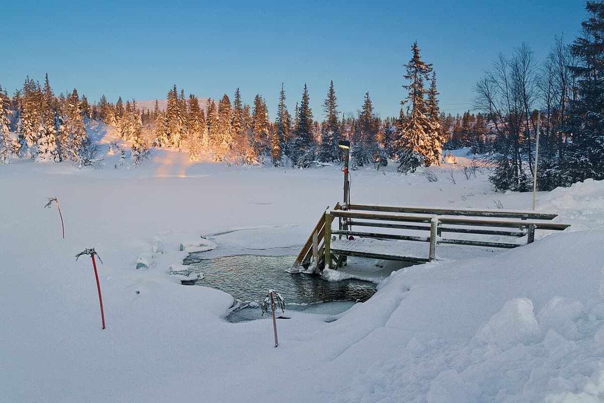 A swimming hole cut in the ice beside a wooden jetty, with low sun on snowy trees